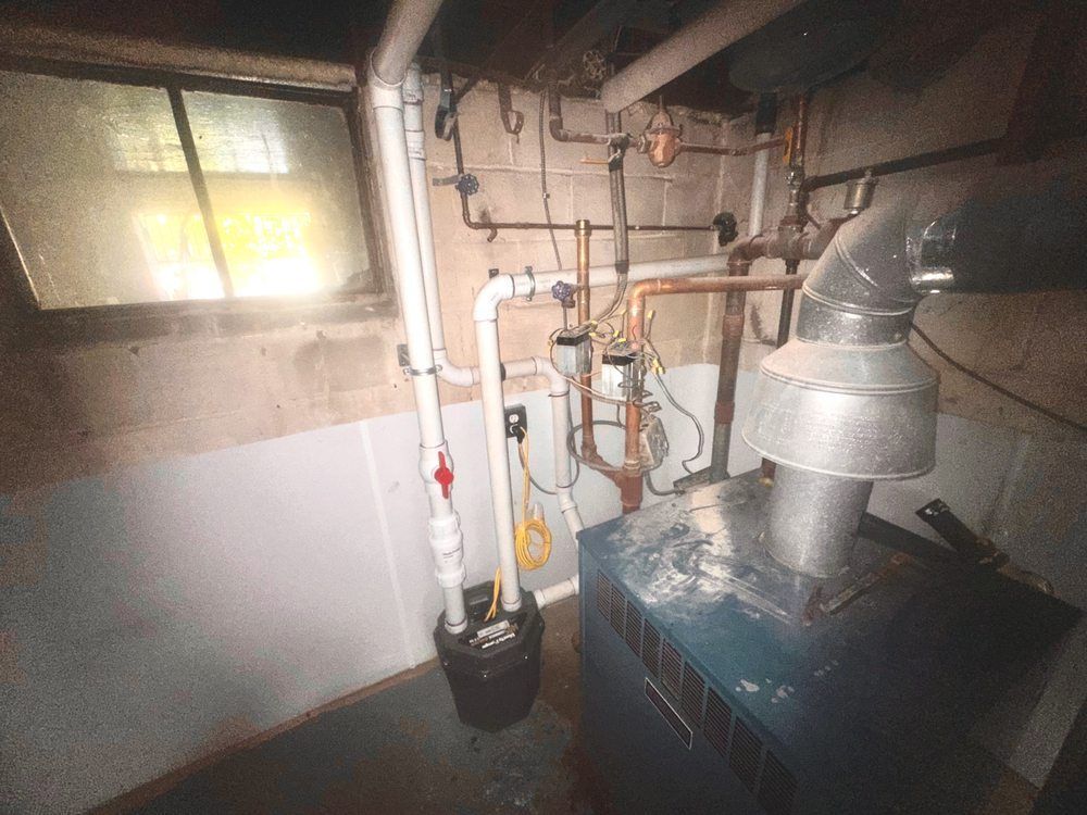 Basement with oil furnace, pipes, sump pump, and a window.