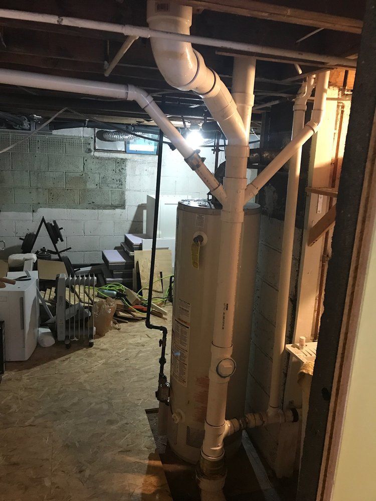 Basement with plumbing around a water heater. White pipes run along the wall.