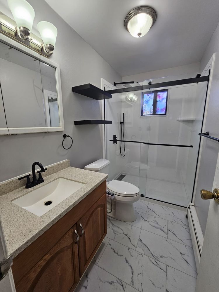 Bathroom with light gray walls, brown vanity, and a glass shower door.
