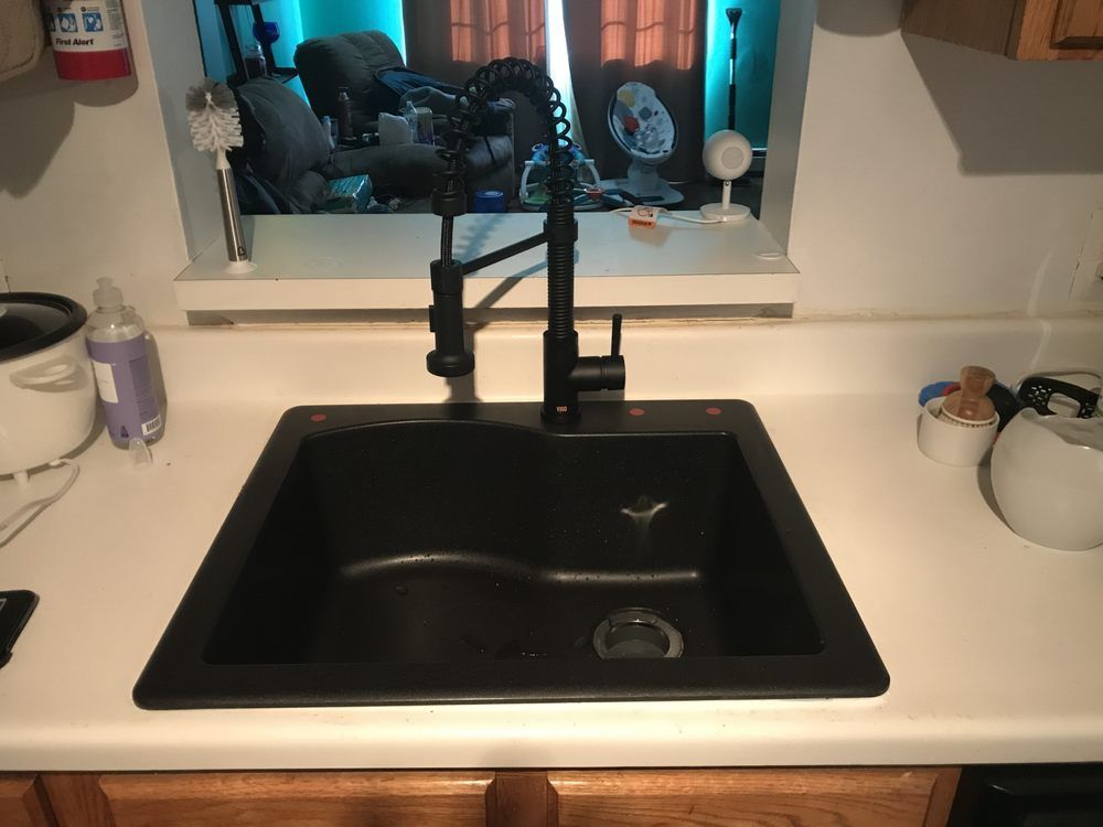 Black kitchen sink with black faucet on white countertop. Window in the background.