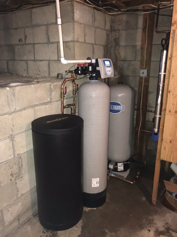 Water softener system in a basement setting with three tanks and copper piping.