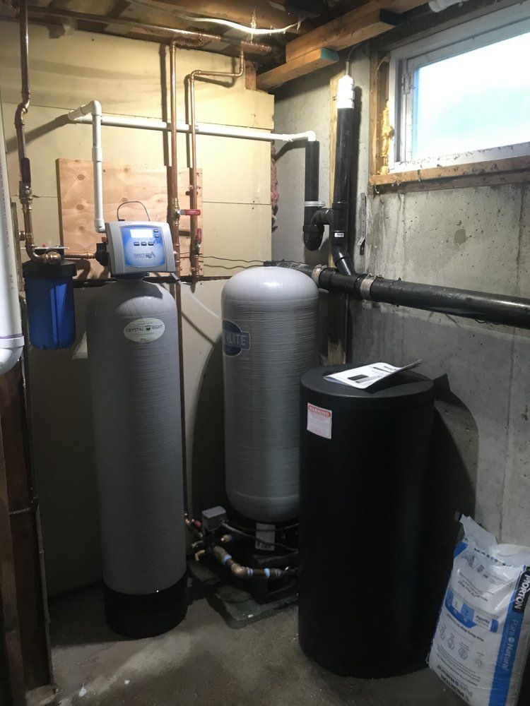 Water treatment system in a basement; gray tanks, blue filter, copper pipes.