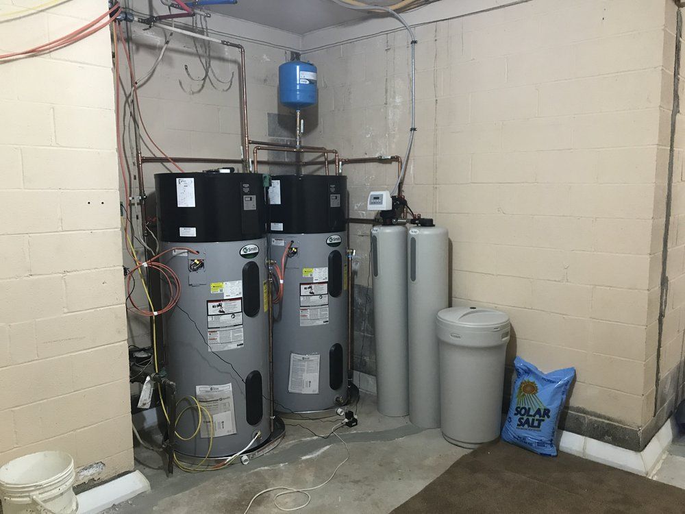 Water heater system in a basement. Two gray tanks, water softener, and a blue expansion tank are present.