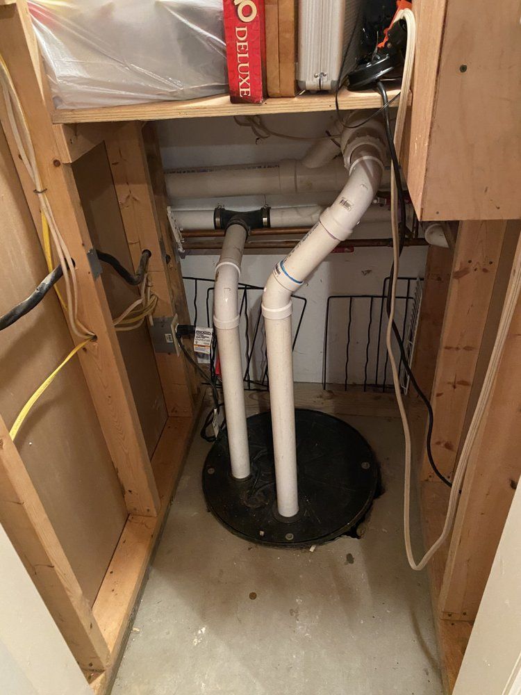 A sump pump in a basement closet with white pipes and exposed framing.