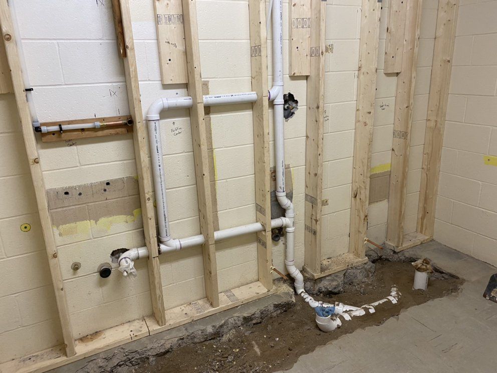 Plumbing pipes installed in the wall studs. A partially finished basement, white pipes, and concrete floor are visible.