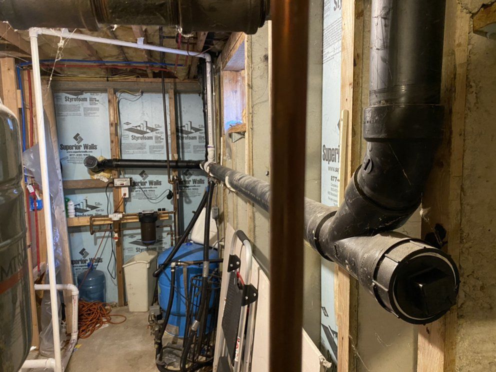 Plumbing pipes in a basement. Black drain pipes attached to a wall, and copper pipes visible.