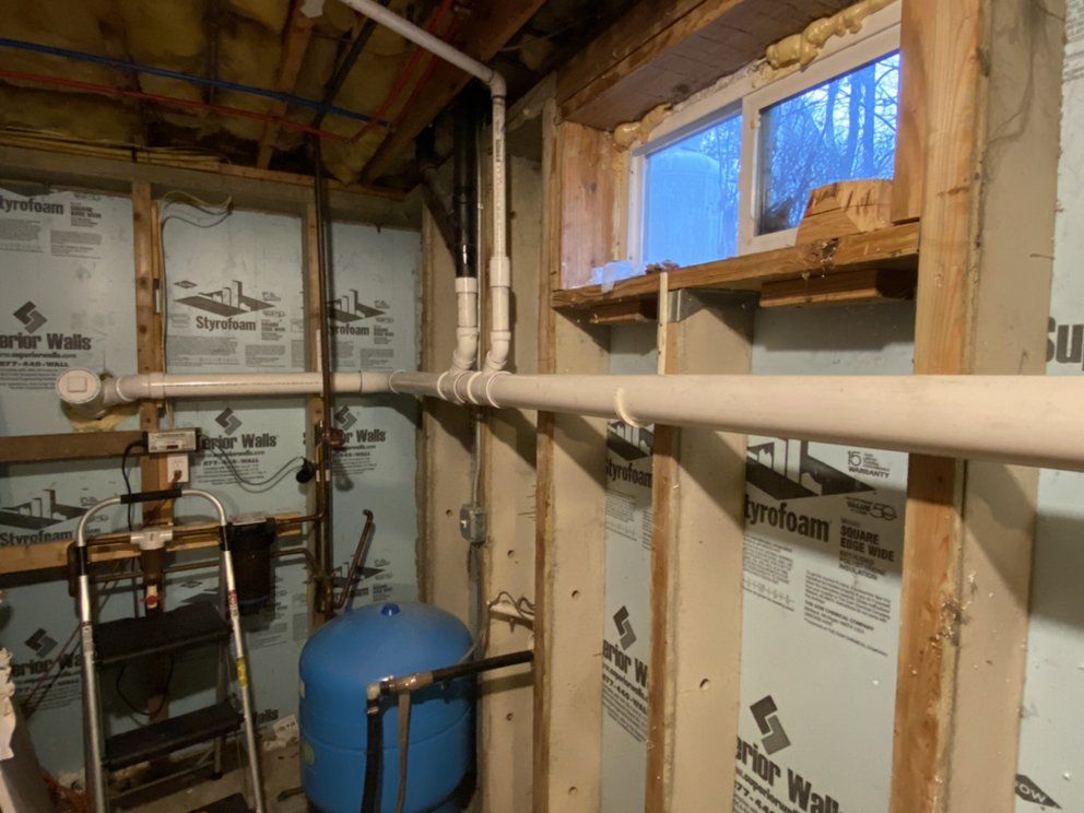 Basement with water pipes, blue pressure tank, window, and insulation.