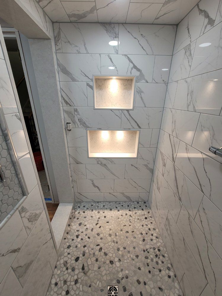 Shower with white marble tile, pebble floor, built-in lit shelves.