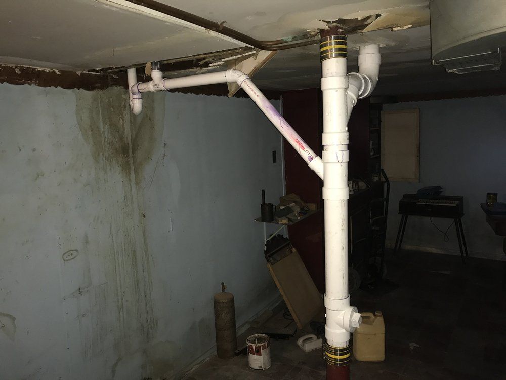 White PVC pipes installed in a basement, possibly for plumbing. Support beam. Dark, dingy walls.