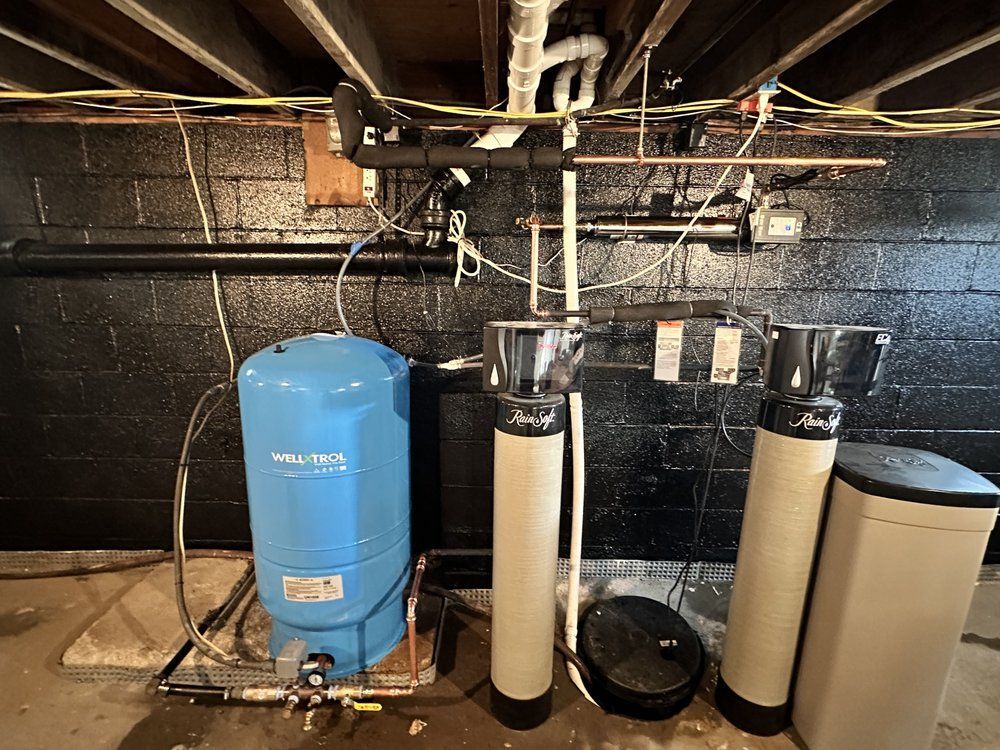 Basement water system: blue pressure tank, filtration columns, and softener against a black painted wall.