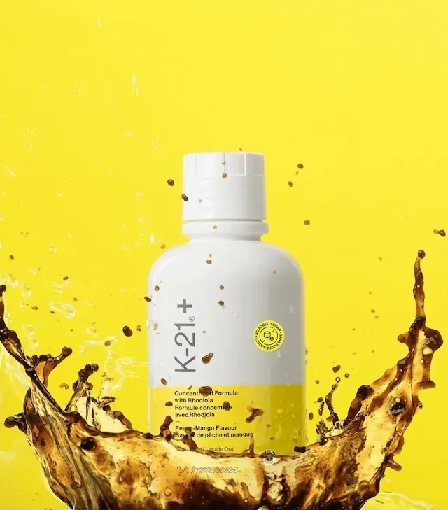 Botella de suplemento líquido K-21+ con etiqueta amarilla, botella y tapa blancas, sobre fondo blanco.