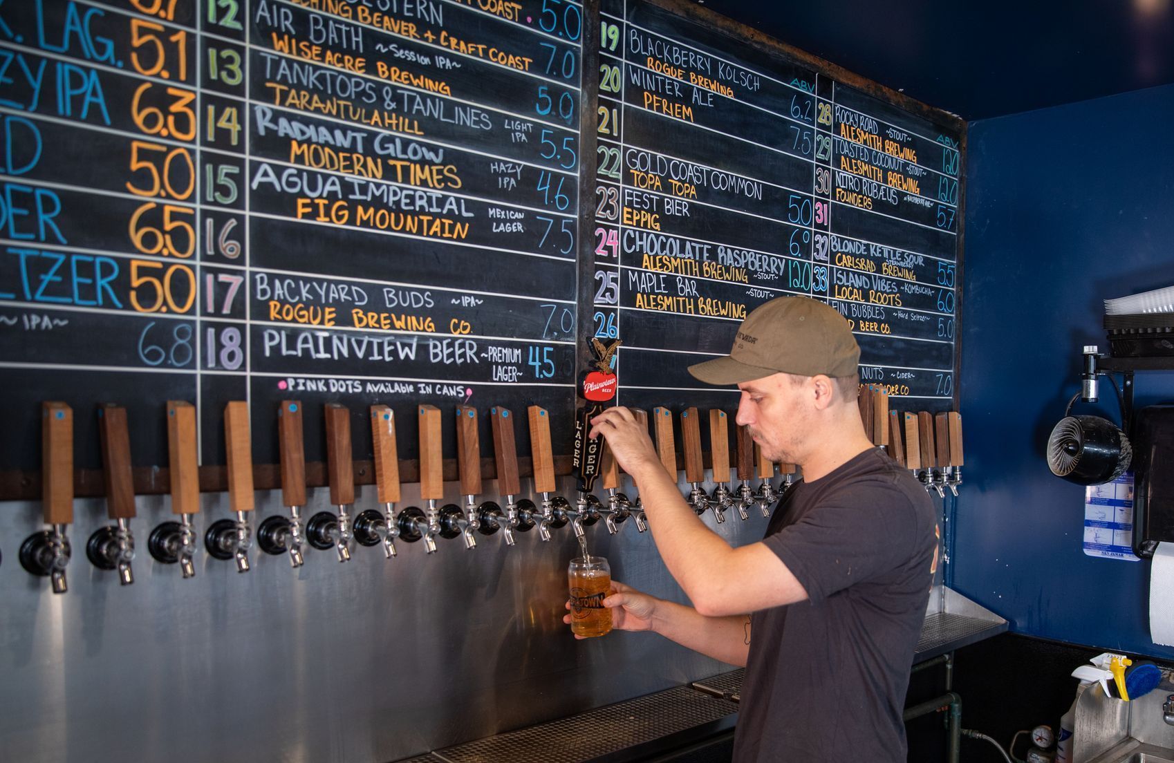 Man pouring beer from a tap at a bar, with a chalkboard menu of beers in the background.