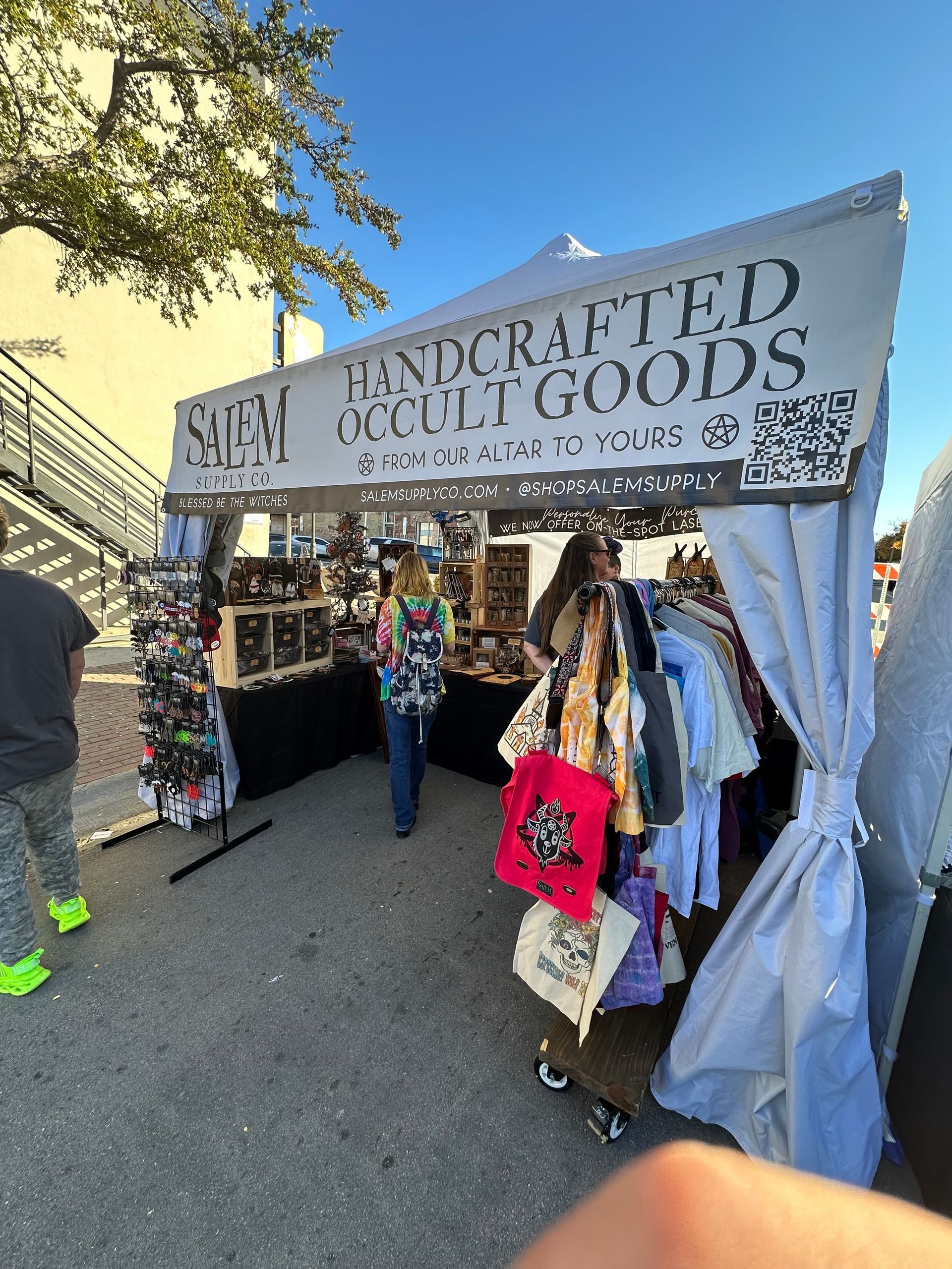 A person is standing in front of a tent that says handcrafted occult goods.