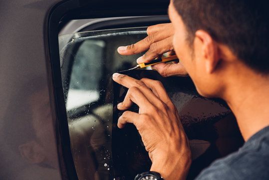 A man is applying tinted window film to a car window.