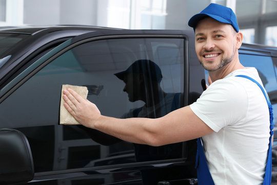 A man is cleaning a car window with a cloth.