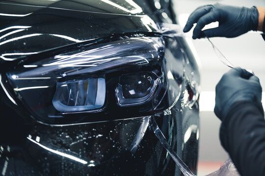 A person is applying a protective film to the headlight of a car.