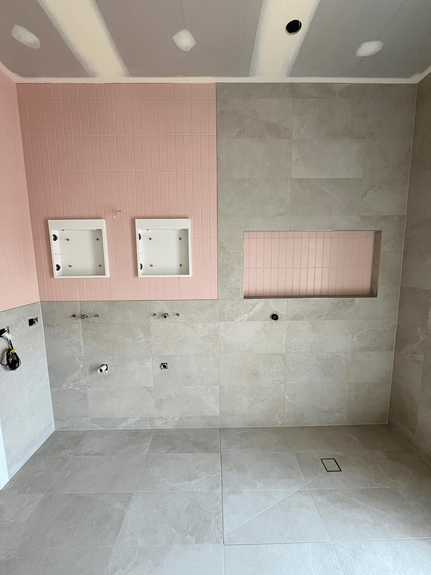 A bathroom under construction featuring large grey floor tiles, grey wall tiles, and accent walls with textured pink tiles.