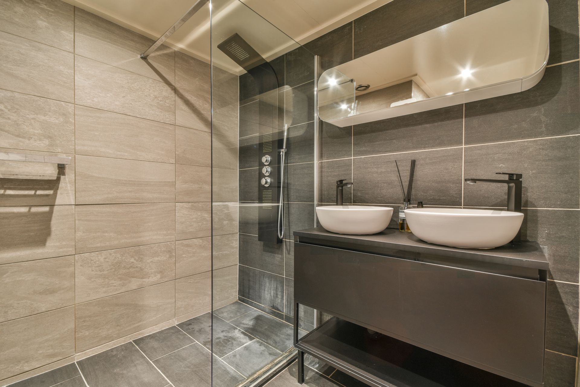 Modern bathroom with a double sink vanity, dark cabinets, a mirror, and a glass-enclosed shower with tiled walls.
