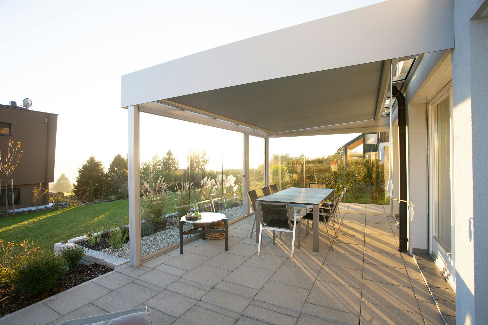 A modern outdoor patio featuring a covered dining area with a table and chairs next to a house under a clear sky.