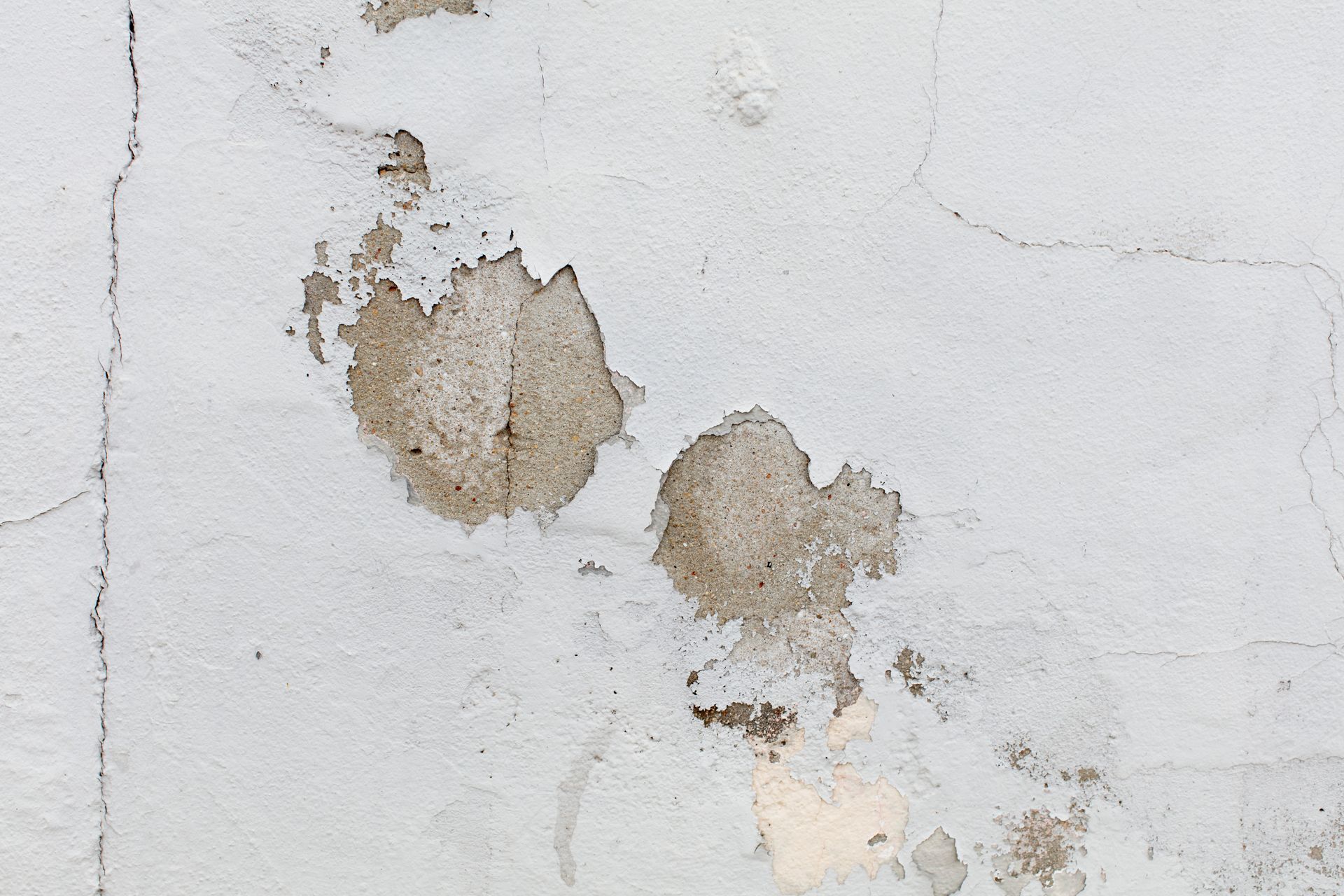 Gray wall with visible cracks and areas of peeling white paint, revealing the rough concrete texture underneath.