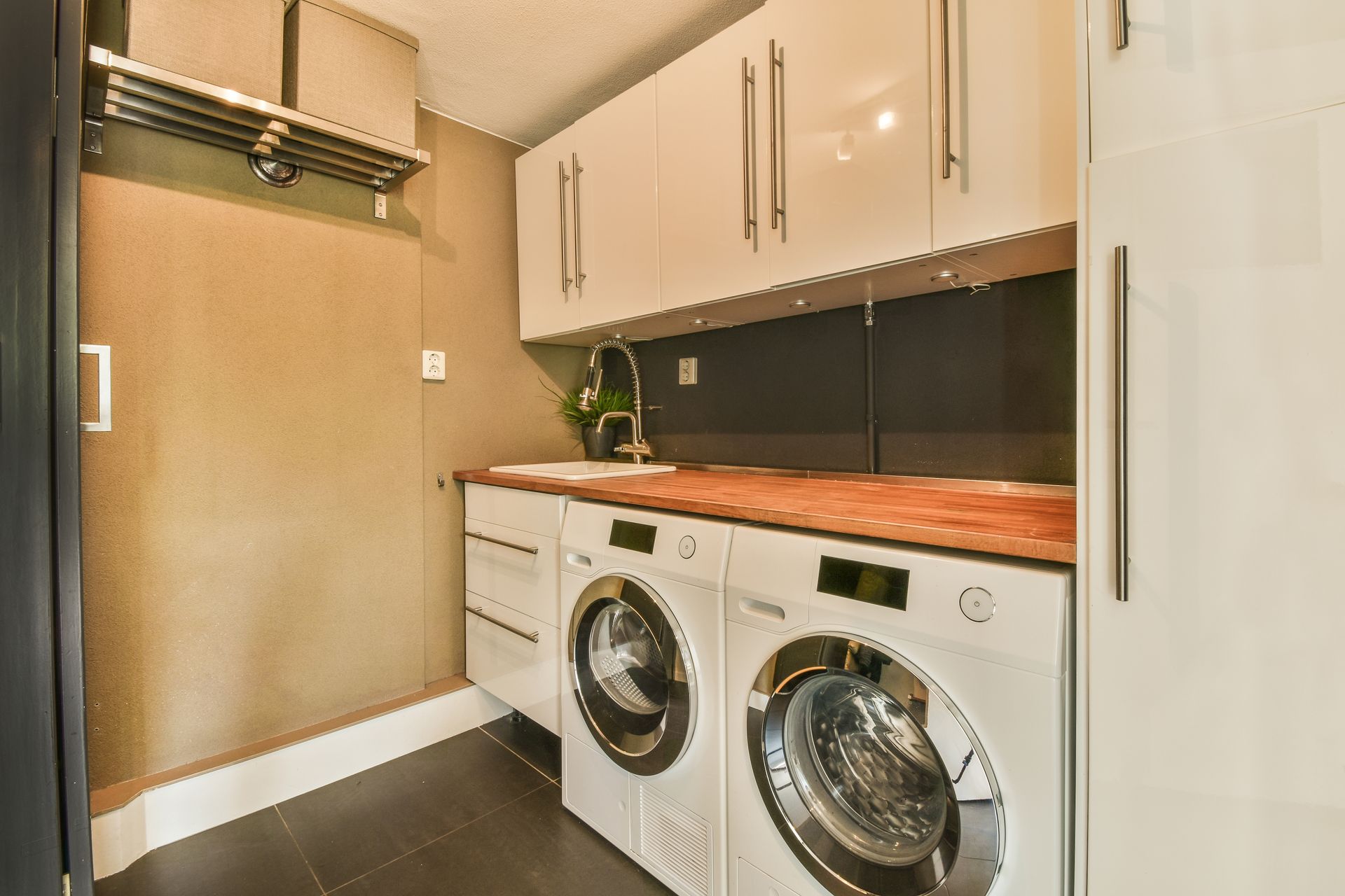Laundry room with white cabinets, wood countertops, two white appliances, and dark tile flooring.