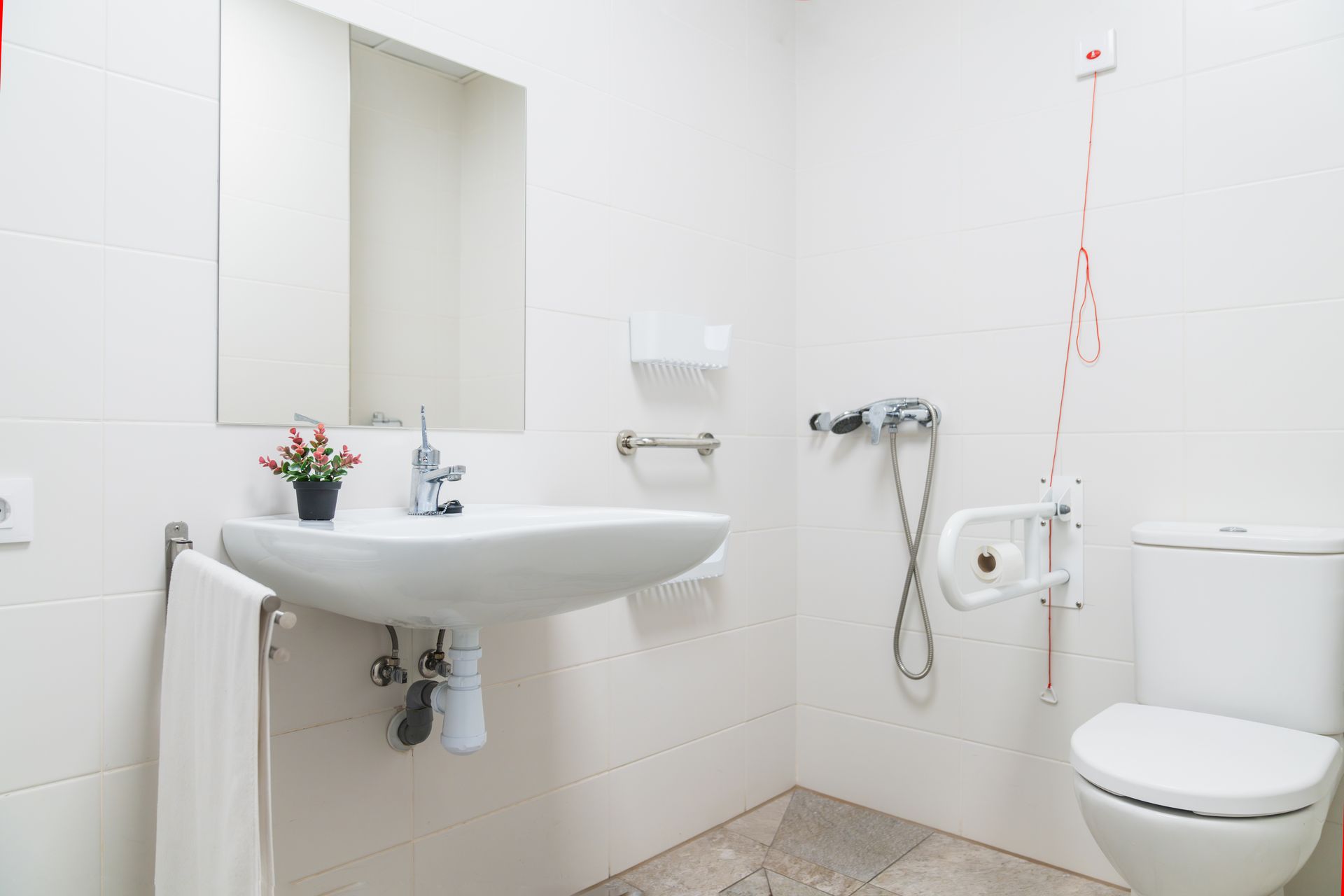 An accessible, all-white bathroom featuring a wall-mounted sink, a mirror, a grab bar, and a toilet with support rails.