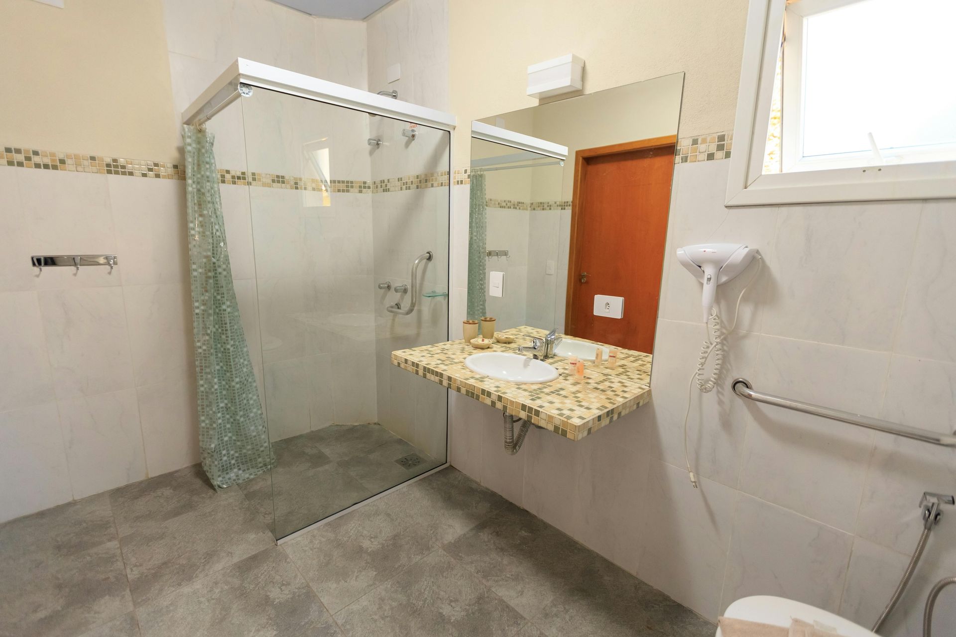 A spacious, accessible bathroom featuring a large walk-in glass shower, a stone-top vanity with a mirror, and grab bars.