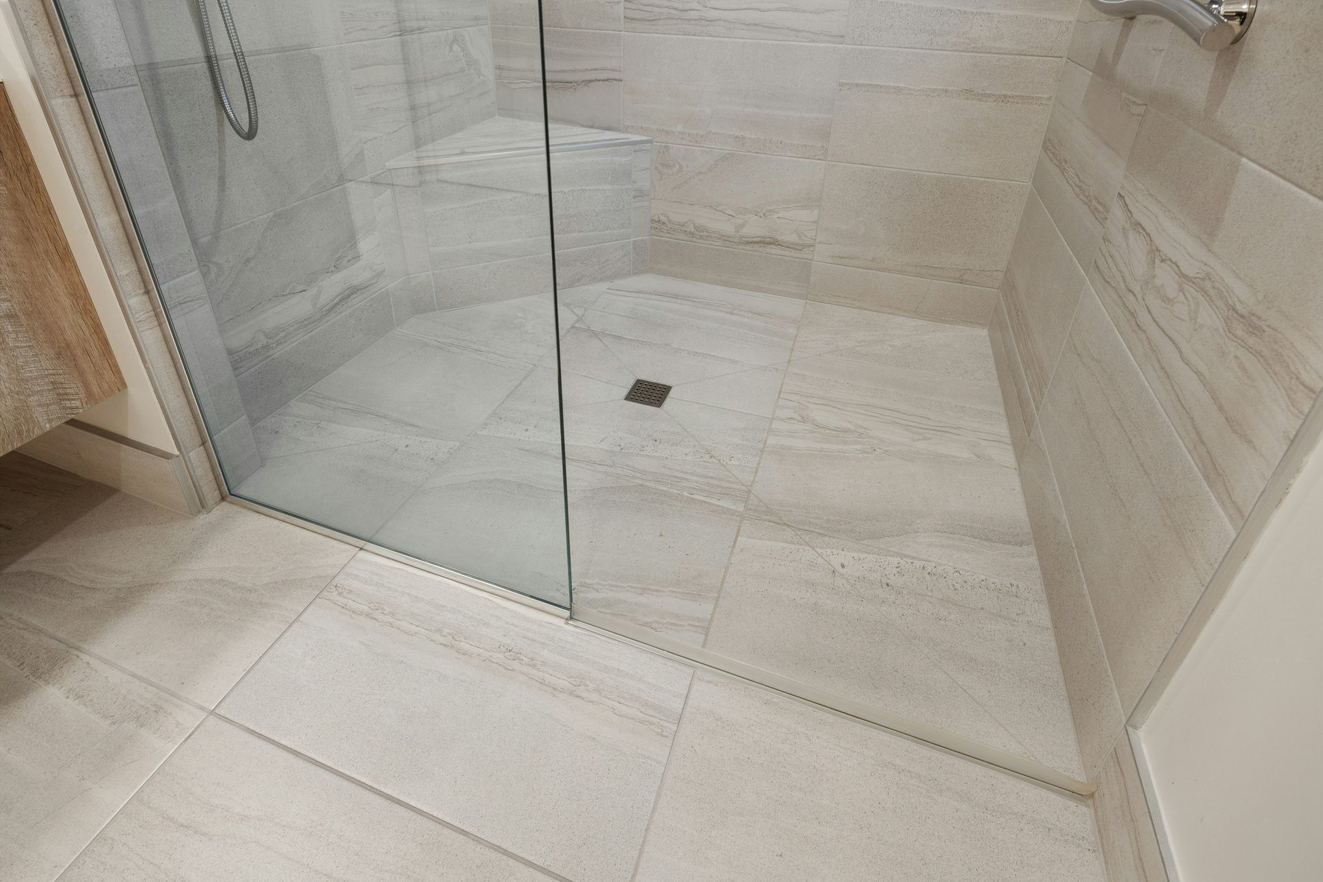 A modern, accessible walk-in shower with light beige stone tiles and a seamless, step-free floor entrance.