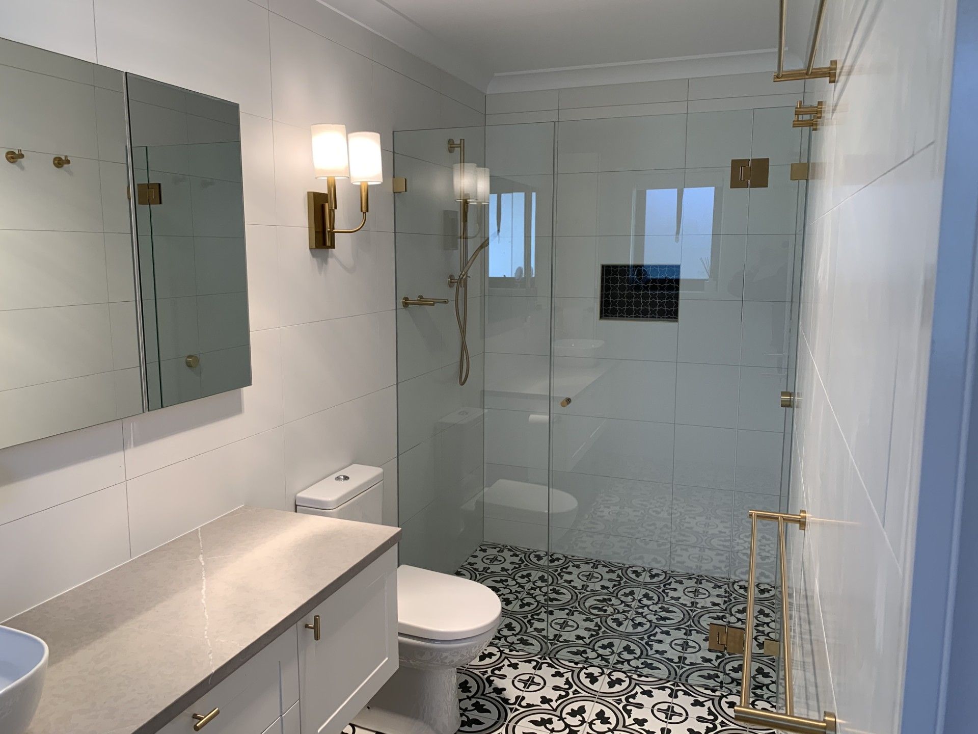 Modern bathroom with white walls, a vanity, a toilet, and a glass-enclosed shower featuring patterned tile flooring.