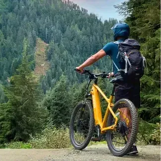 A man is riding an electric bike on a dirt road in the woods.