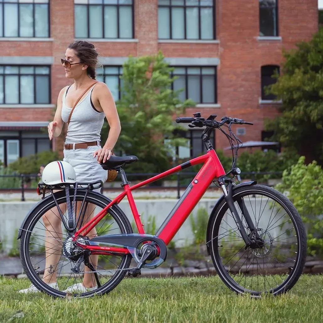 A woman is standing next to a red bicycle in the grass.