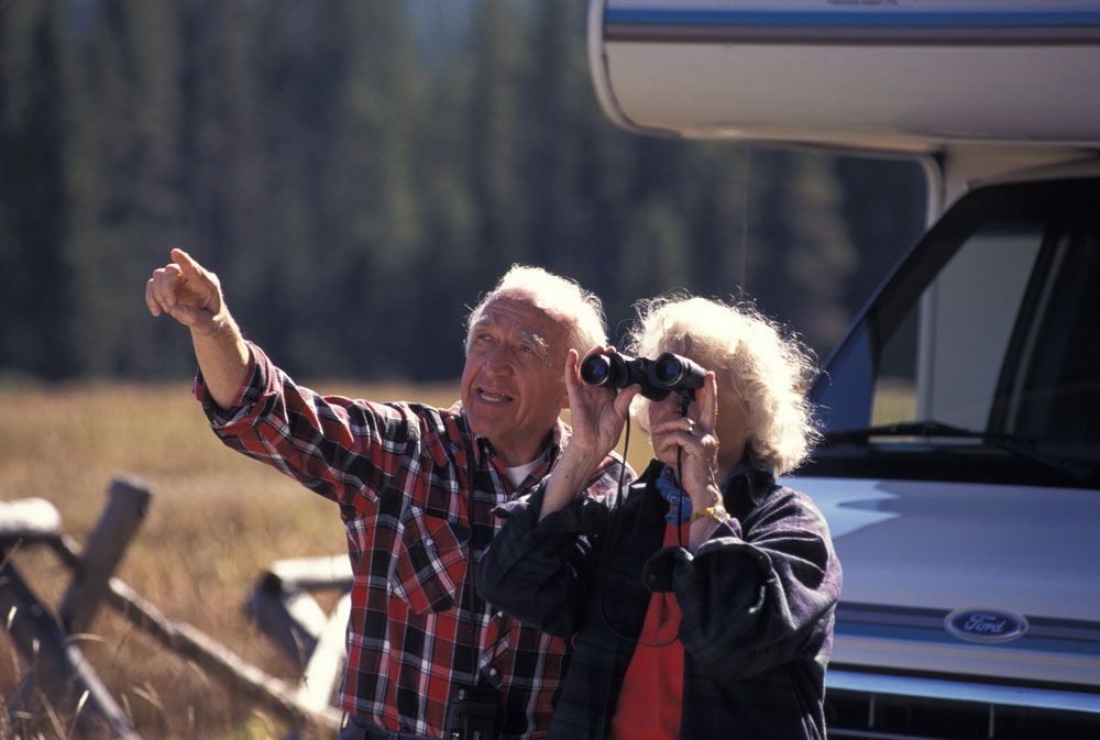 A man and a woman are looking through binoculars in front of a ford van.