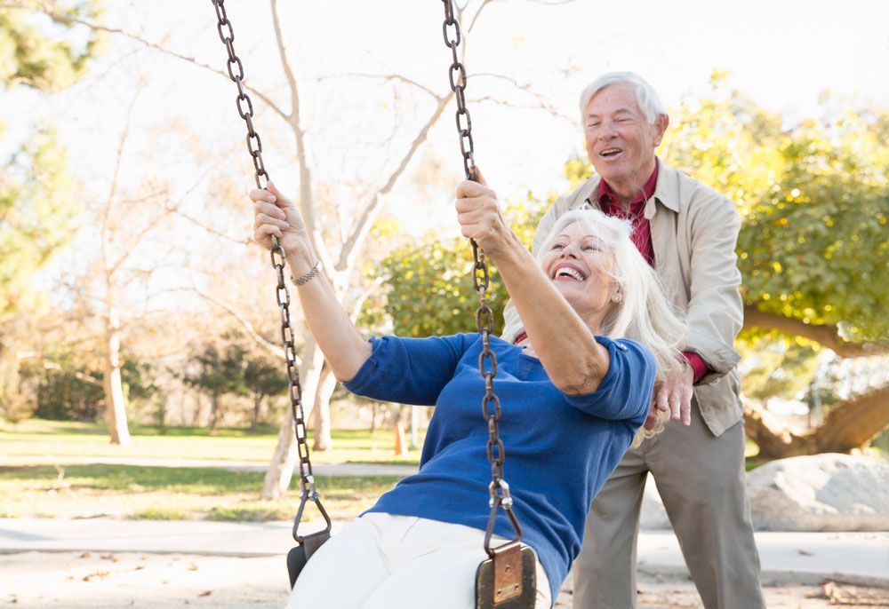 An elderly couple is playing on a swing in a park.