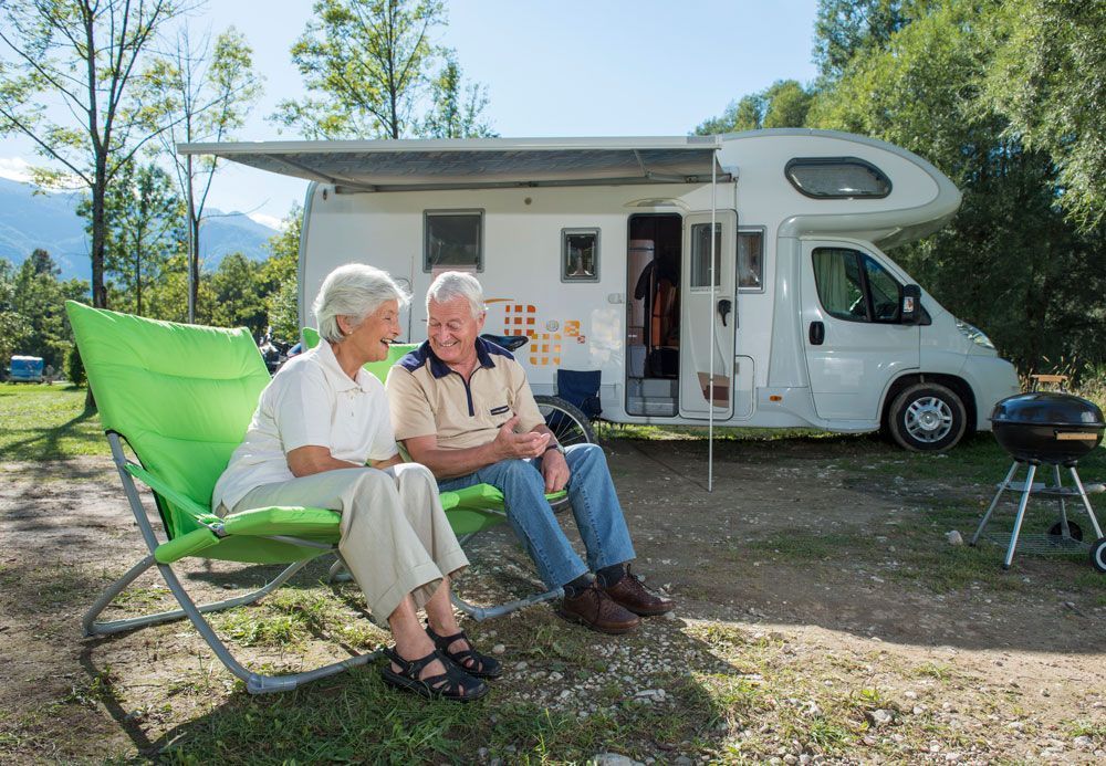 An elderly couple is sitting on a bench in front of a rv.