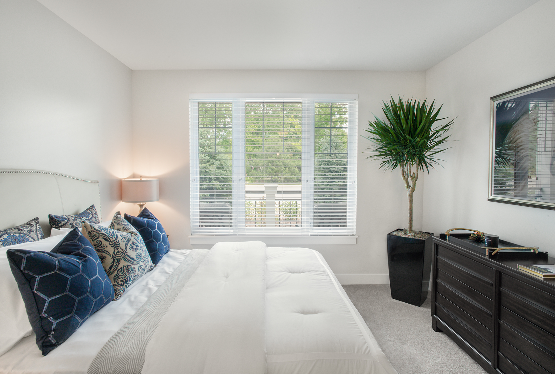 A bedroom with a bed , dresser , lamp and window.