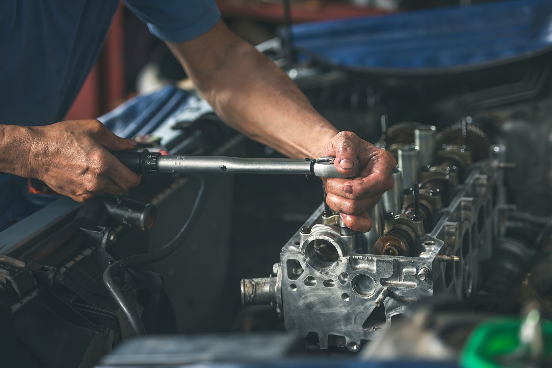 Mechanic uses a wrench to work on a car engine in a garage setting.