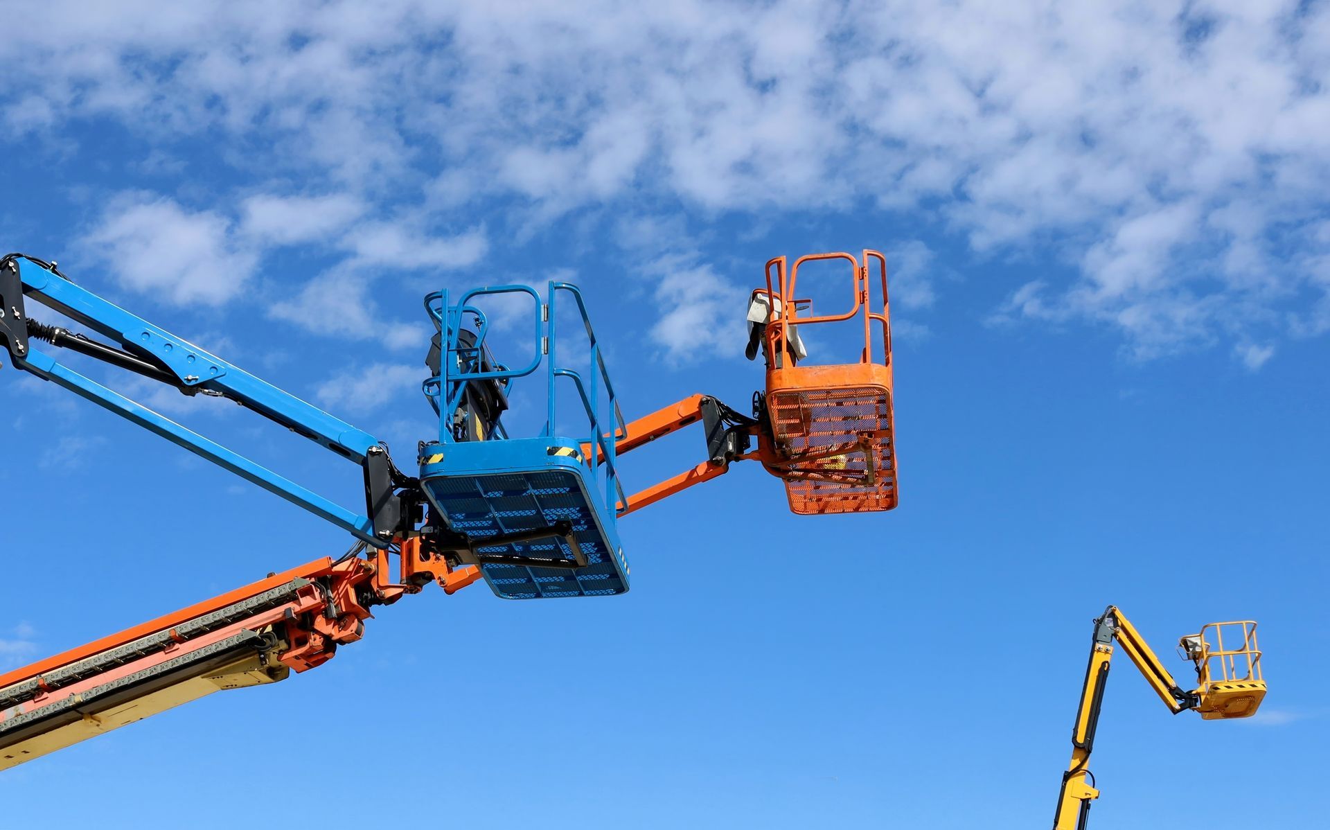 Aerial lifts with workers in baskets against a blue sky with clouds.