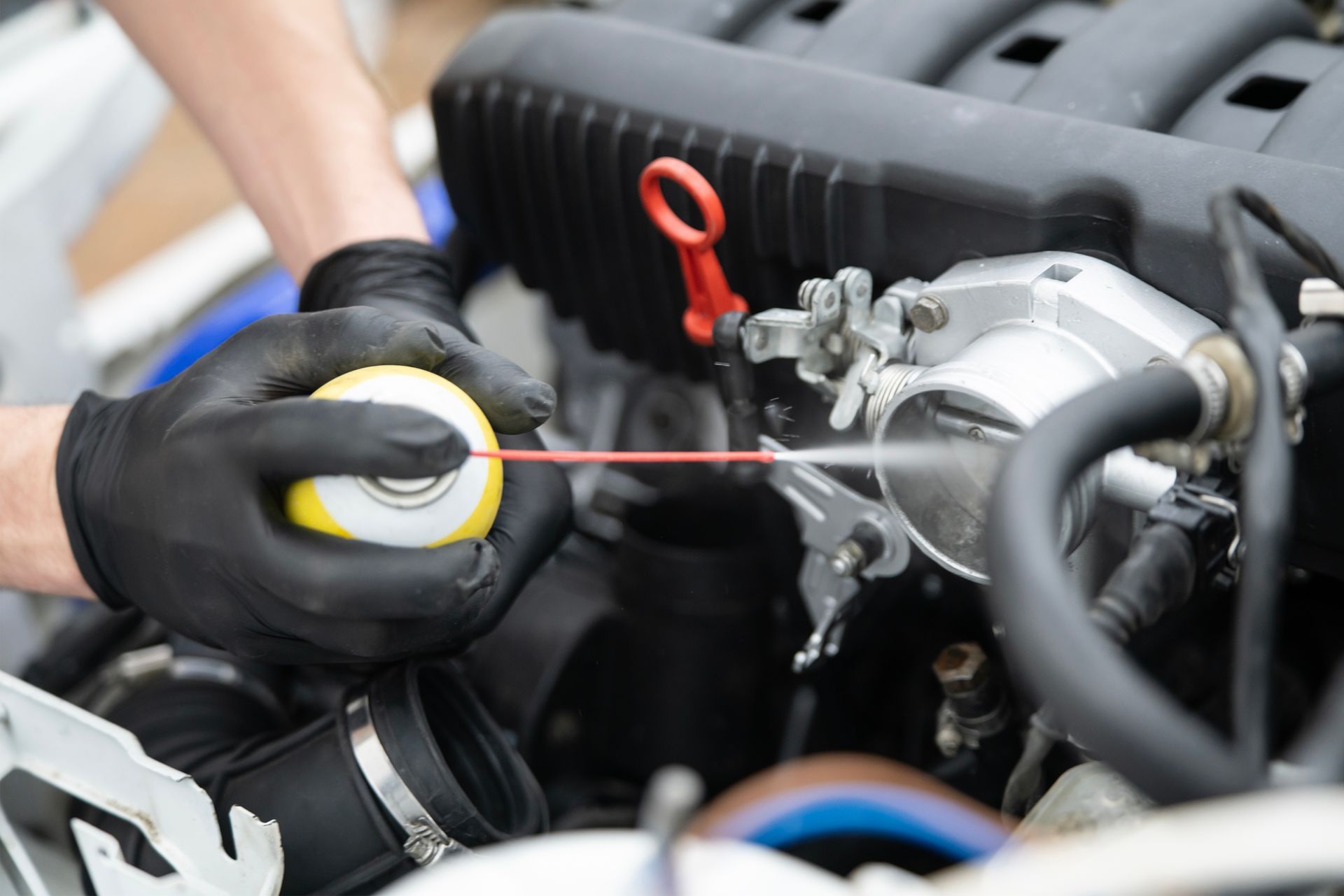 Person in black gloves sprays cleaner on a car engine component.
