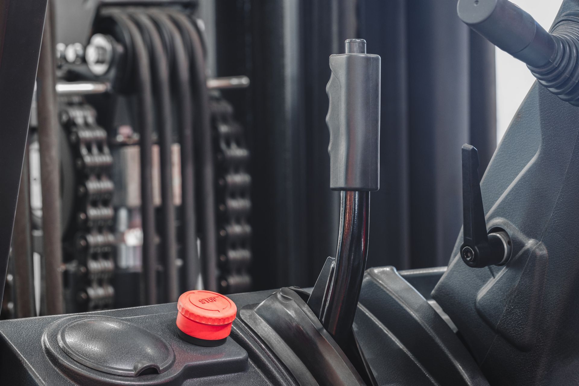 Close-up of a forklift control panel with a red emergency stop button, gear shift lever, and other controls.