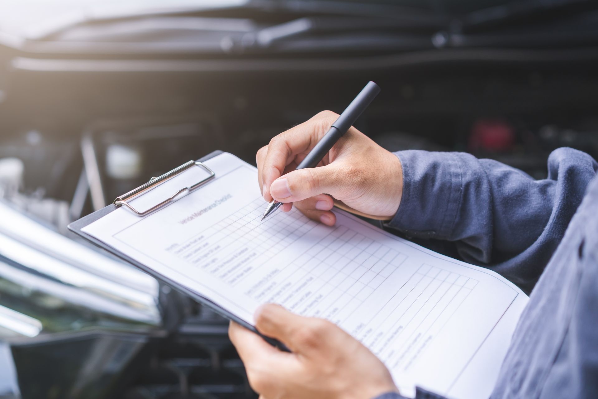 Mechanic writing on clipboard while inspecting a car engine.