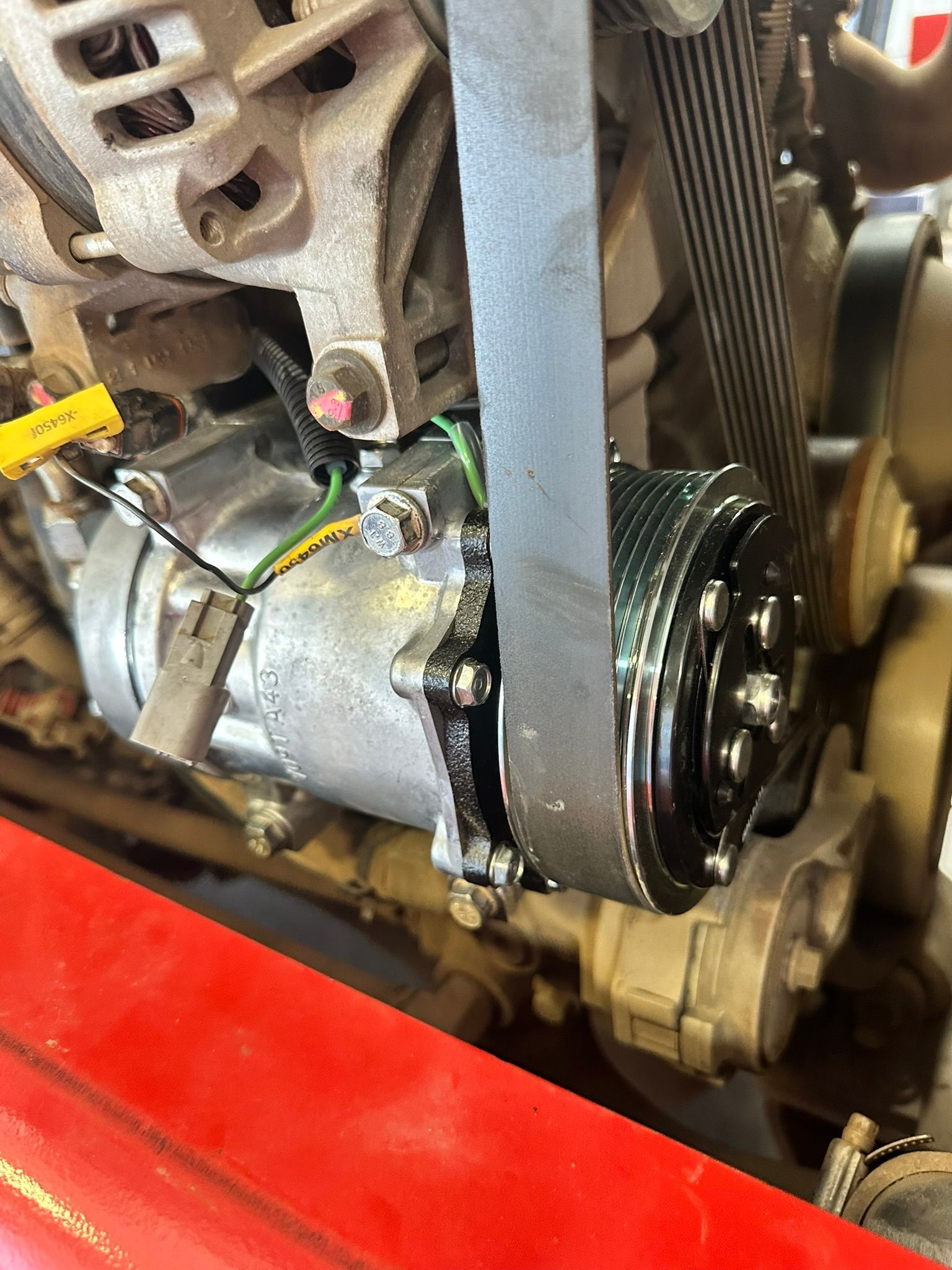 Close-up of a vehicle engine with a belt wrapped around a compressor, showing mechanical components.