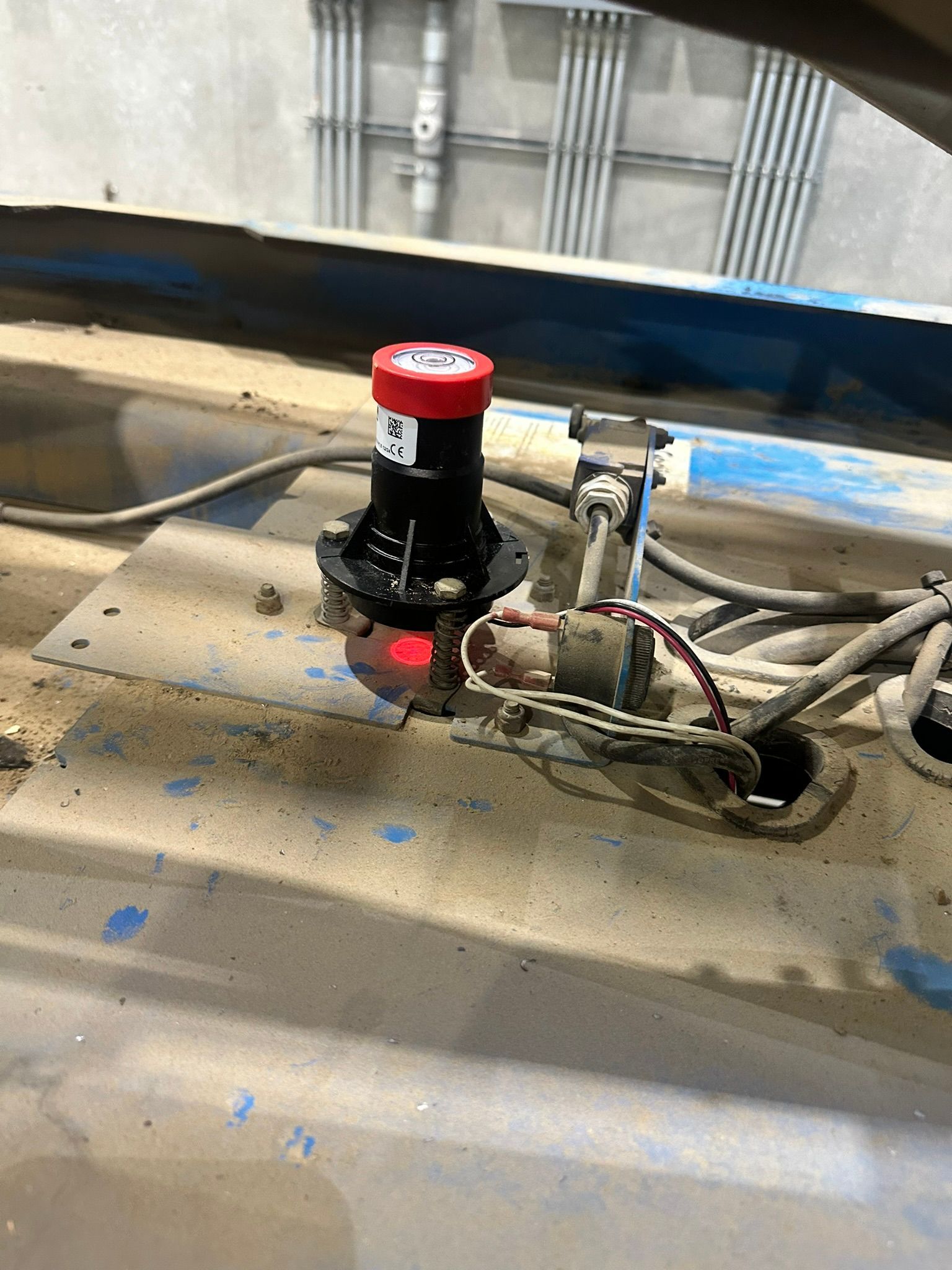 Close-up of a red emergency stop button with an indicator light on a dusty metal surface, possibly on machinery.