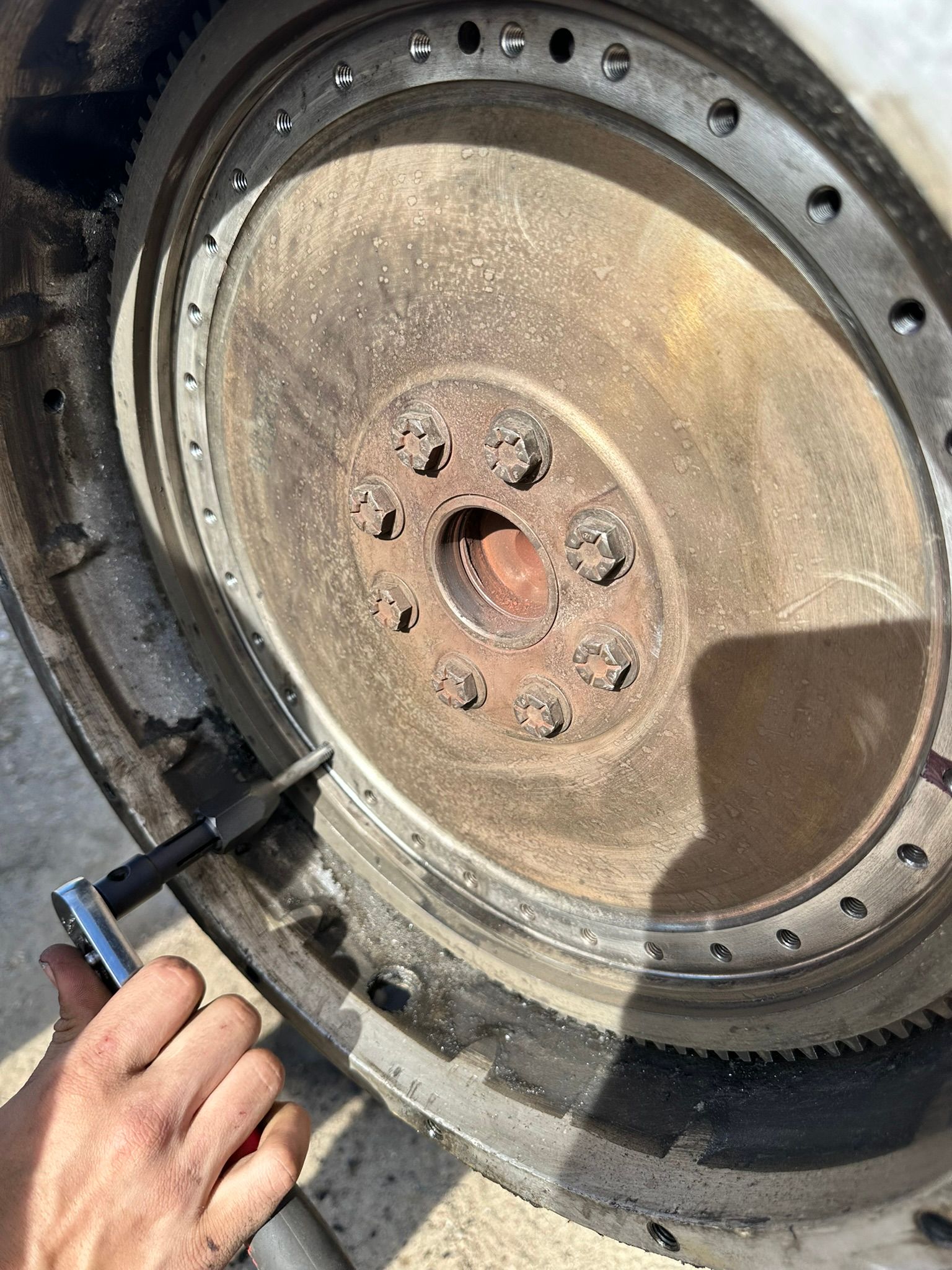 A person uses a wrench on a flywheel, likely for a vehicle repair.