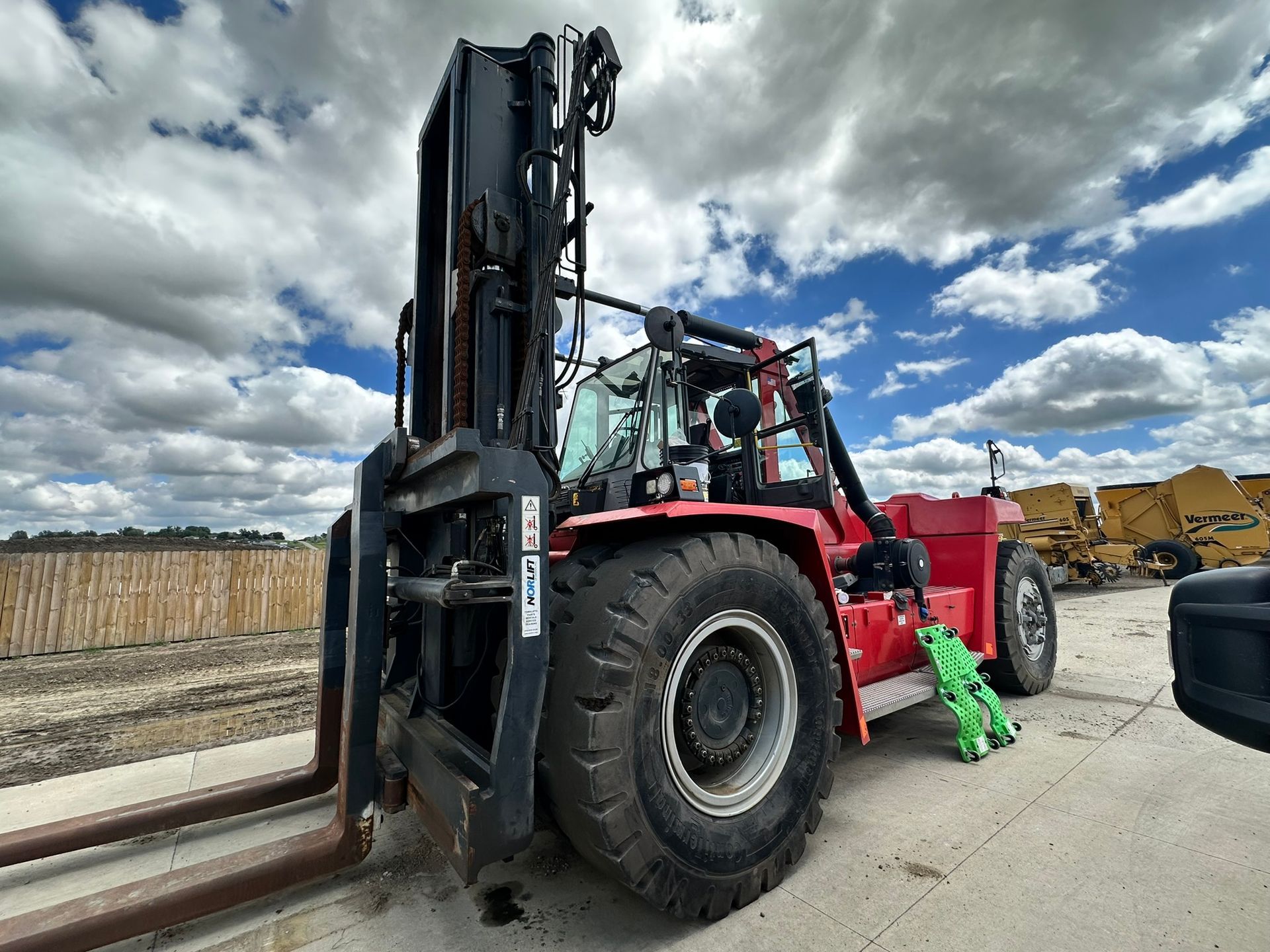 Red forklift with large tires on a cloudy day.