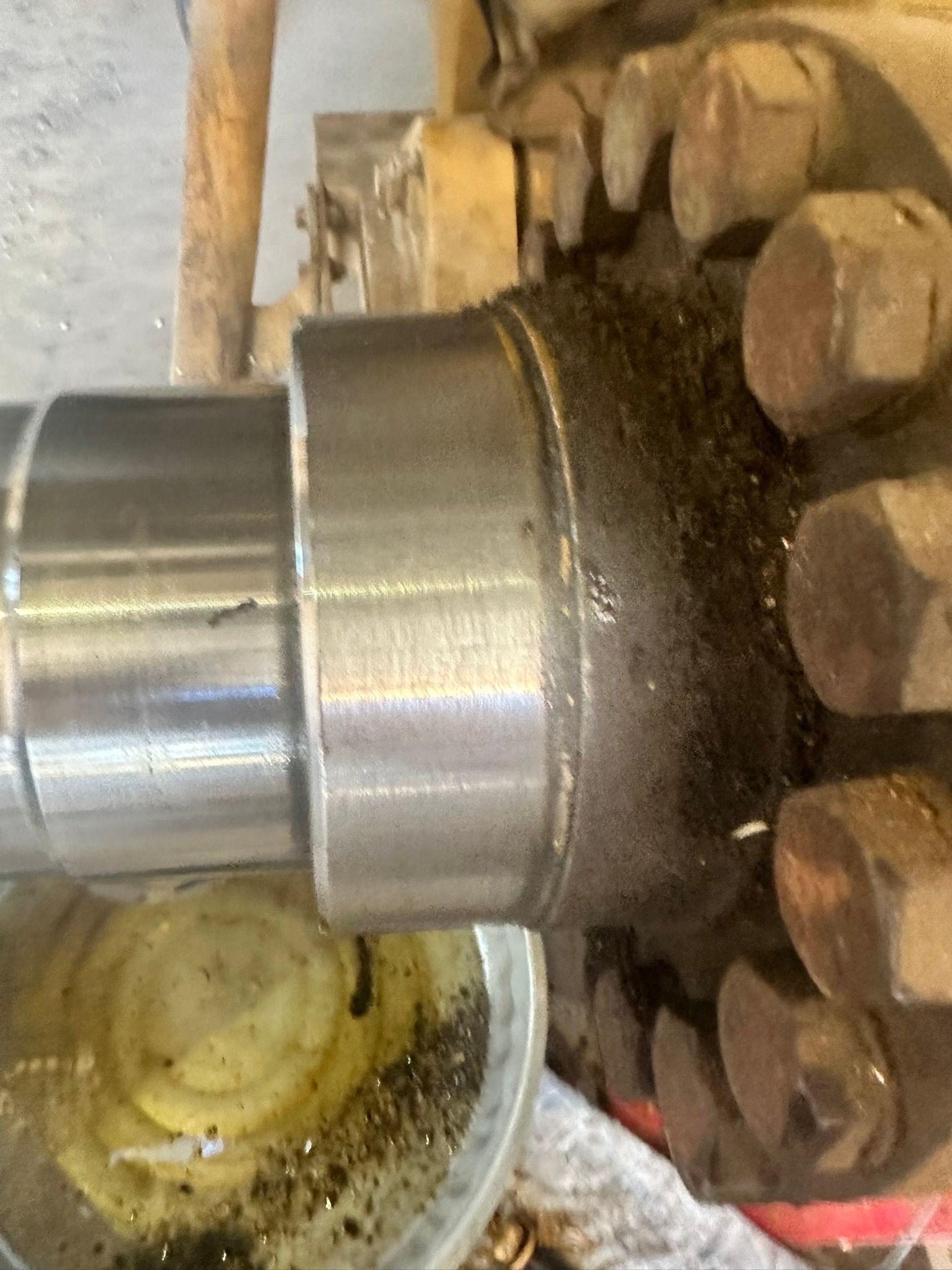 Metal shaft with oily, dirty coupling, bolts, and surrounding debris.