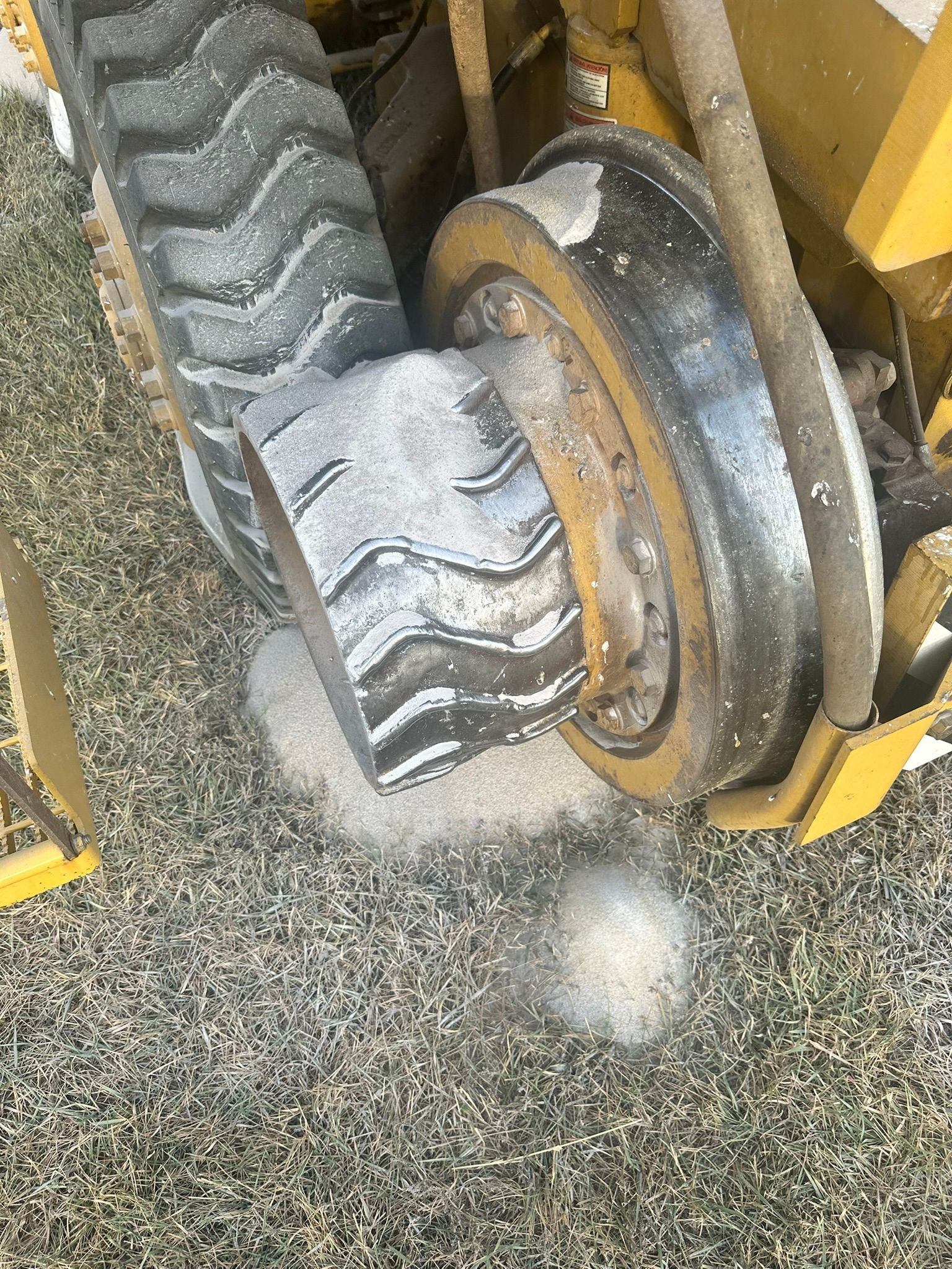 Yellow tracked machine grinding a stump, sawdust on the ground.