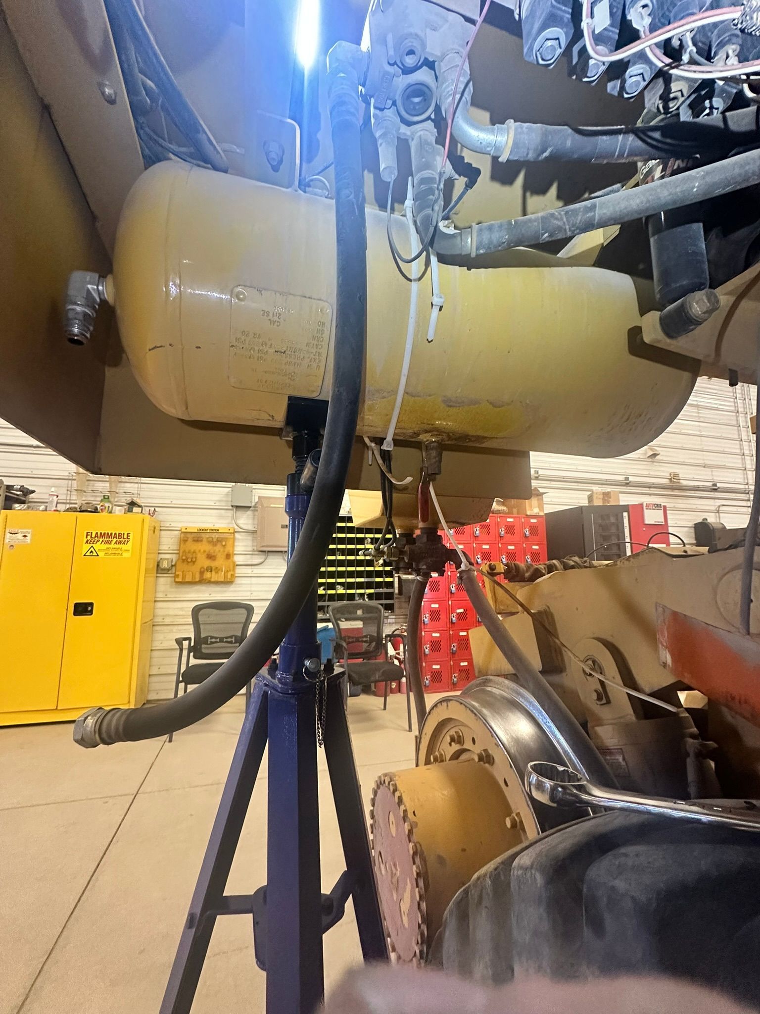 Yellow air tank attached to a vehicle with hoses and other mechanical components in a workshop.