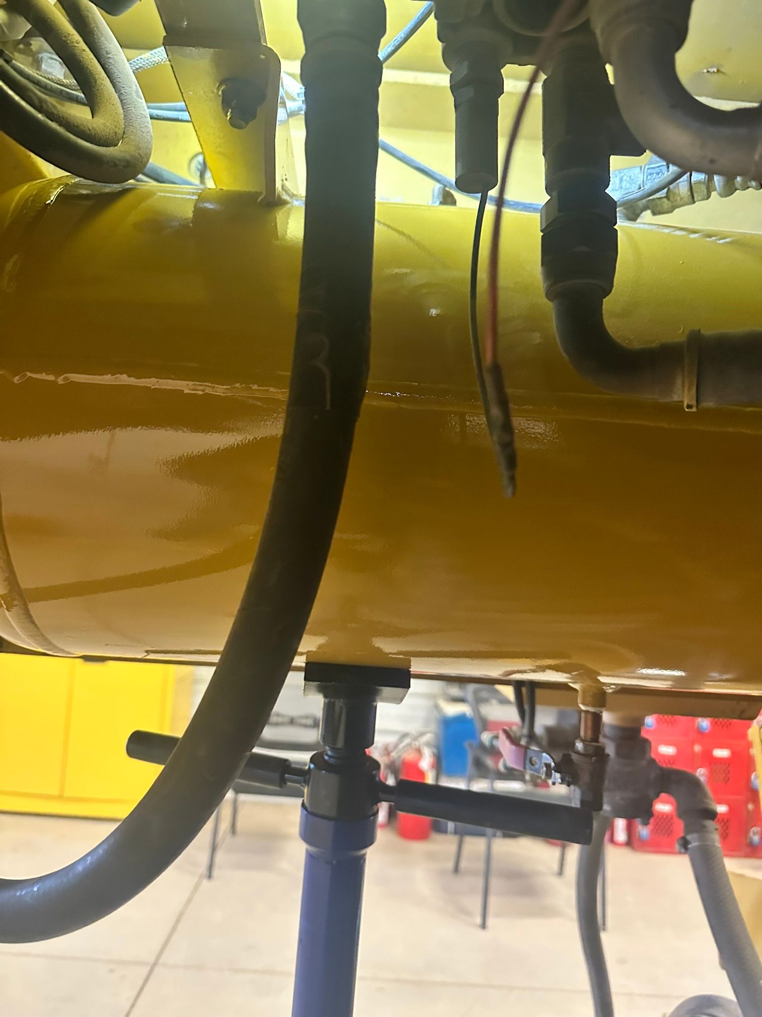 Yellow industrial tank with black hoses and a blue stand, in a workshop setting.