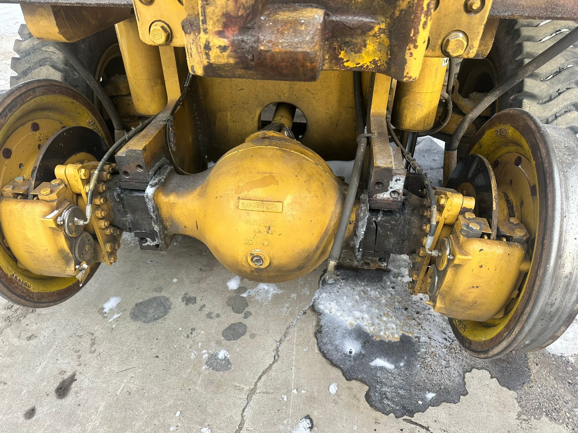 Yellow and black tractor rear axle with wheels on a concrete surface.