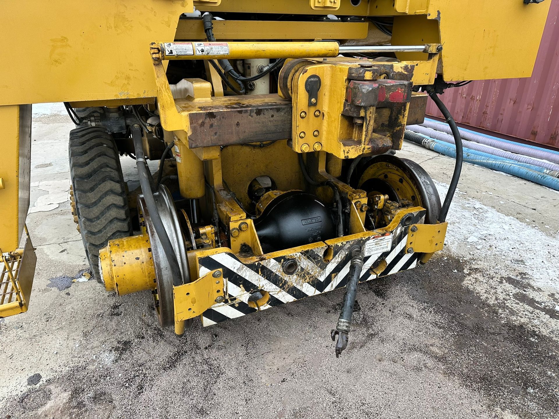 Yellow railway maintenance machine with wheels and black/white striped safety markings.
